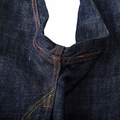 Close-up of dark indigo denim fabric showing the waistband and center seam with contrasting orange and yellow stitching. Shows bartack reinforcement stitching at 3 points on the crotch seam area.