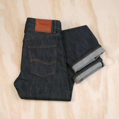 Folded indigo selvedge jeans showing the back pocket, leather patch and turned-up selvedge hems.