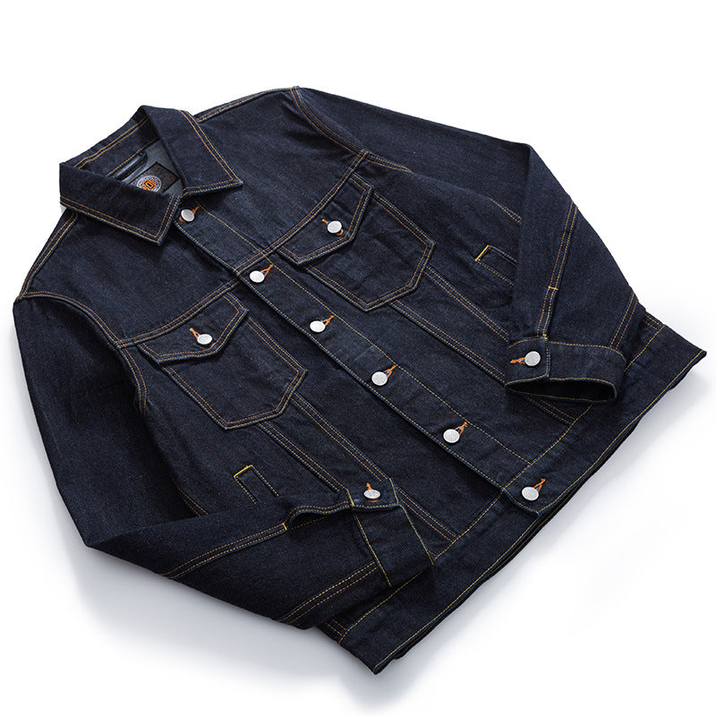 A dark indigo selvedge denim jacket with contrasting  orange stitching and silver metal snap buttons, laid flat on a white background.