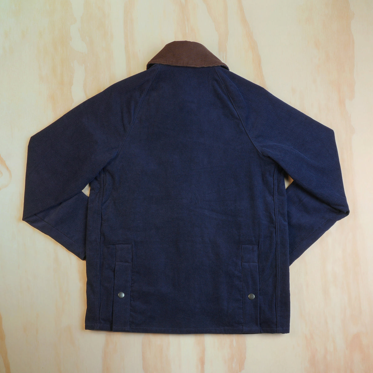 Back view of the navy corduroy hunting jacket showing raglan sleeves and rear hem snaps.