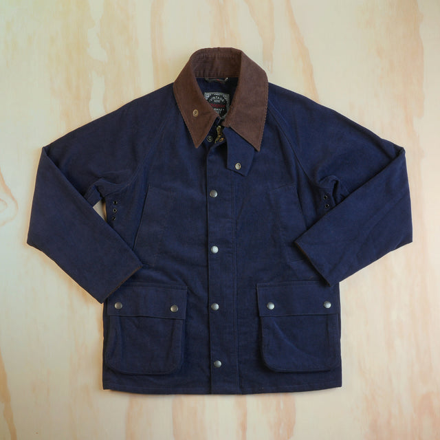 Front view of the navy corduroy hunting jacket with brown collar, snap storm flap and lower flap pockets, laid flat.