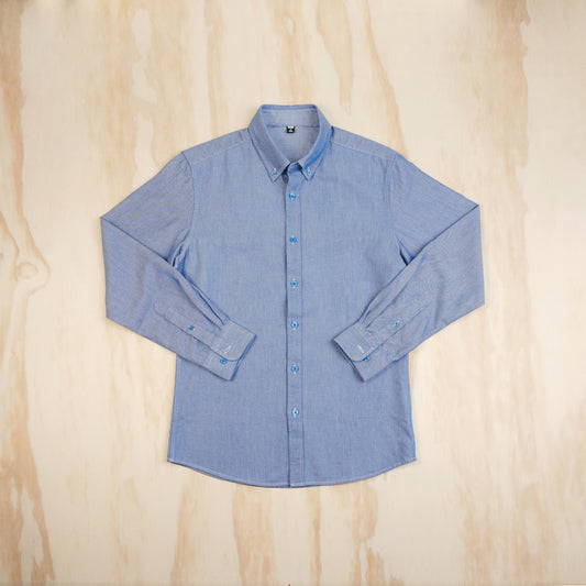 A light blue long-sleeve button-up oxford cloth shirt laid flat on a light wood background, viewed from the front.