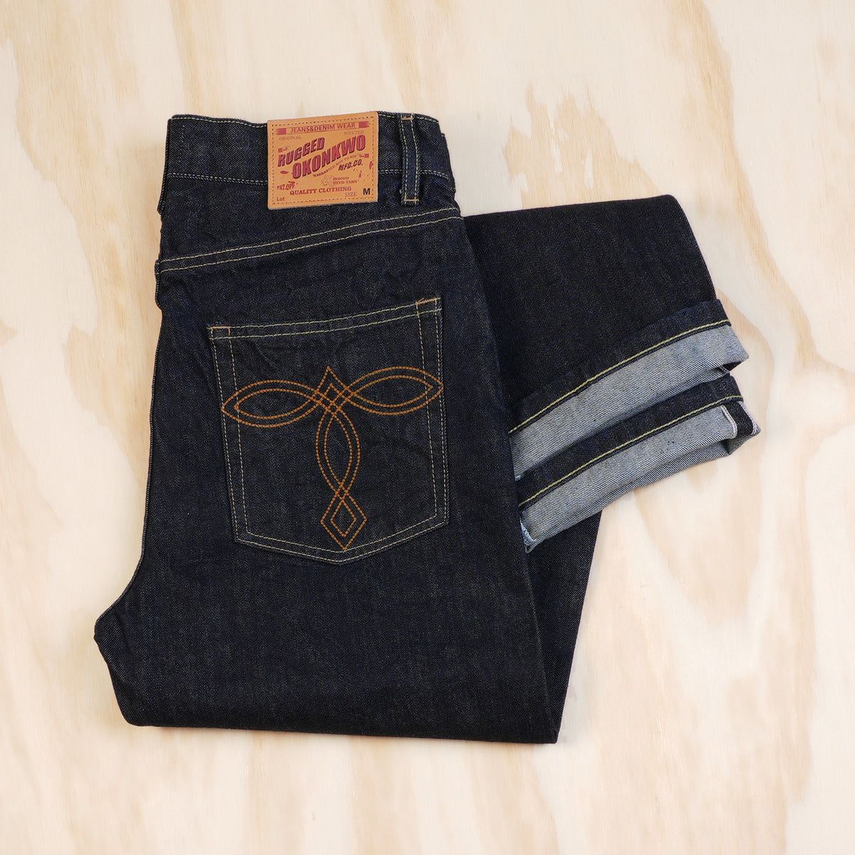 Folded OKONKWO jeans showing the leather patch, pocket embroidery and redline selvedge