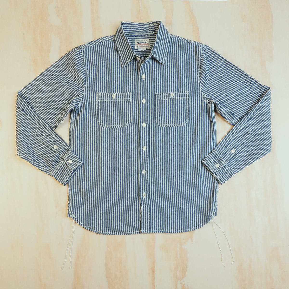 Front of the OKONKWO blue and ecru hickory stripe cotton work shirt, laid flat with two chest pockets.