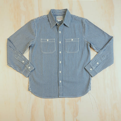 Front of the OKONKWO blue and ecru hickory stripe cotton work shirt, laid flat with two chest pockets.