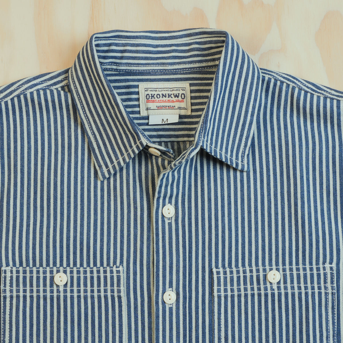 Point collar, OKONKWO neck label and cream buttons on the blue and ecru hickory stripe shirt.