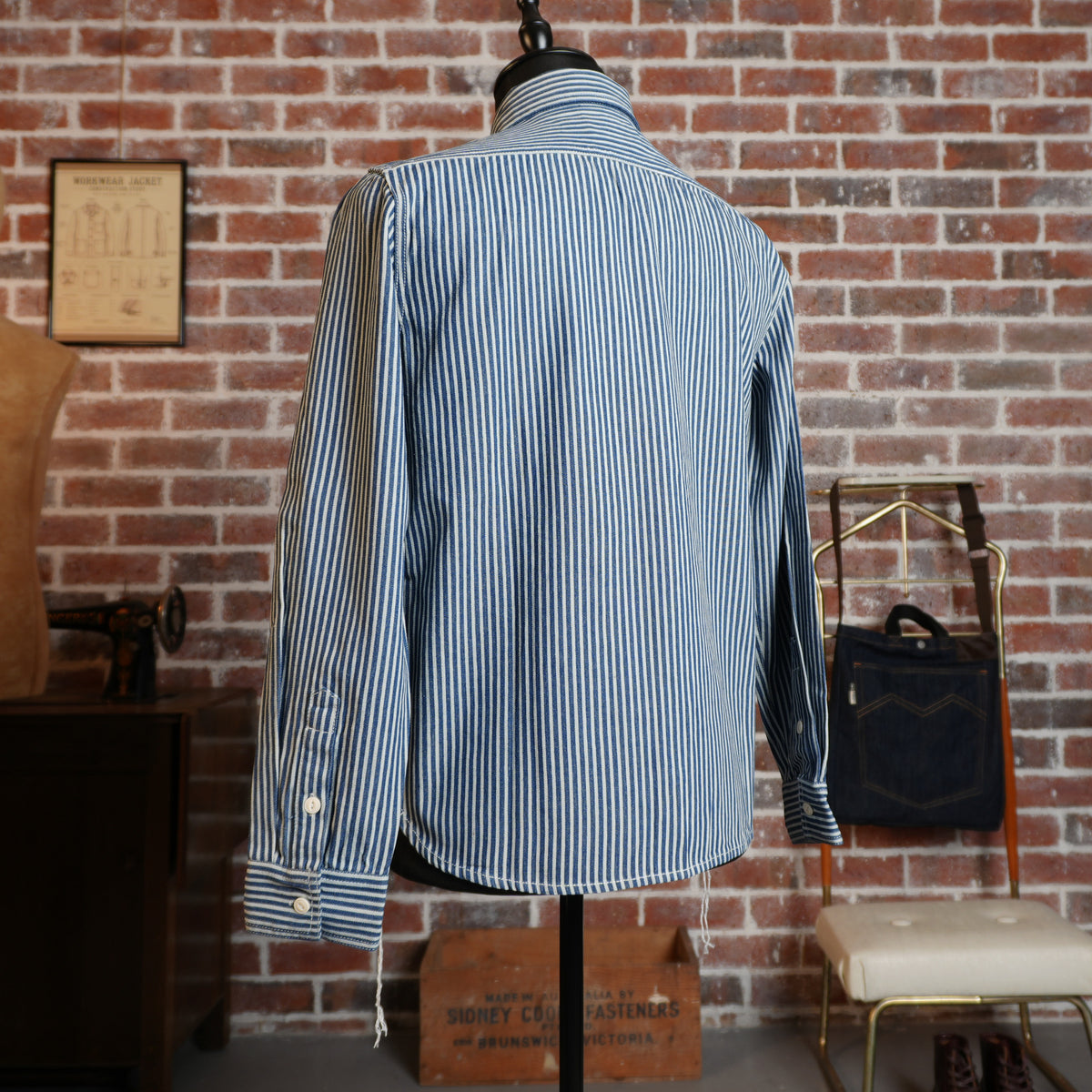 Back view of the hickory stripe cotton work shirt on a mannequin, showing the yoke, cuffs and curved hem.