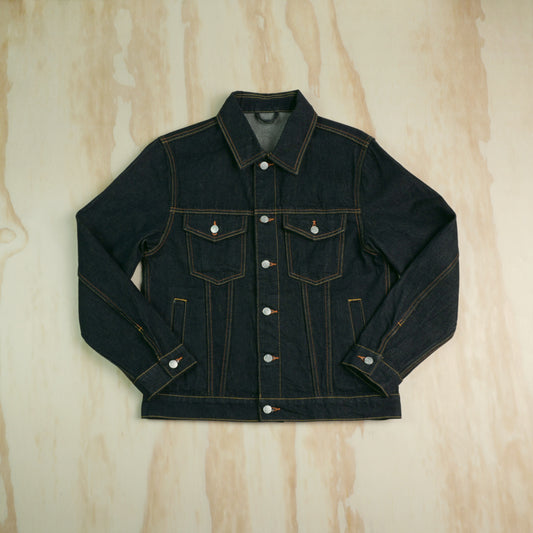 A dark indigo type 3 selvedge denim trucker jacket with contrast gold/yellow stitching, laid flat on a light wood grain background.