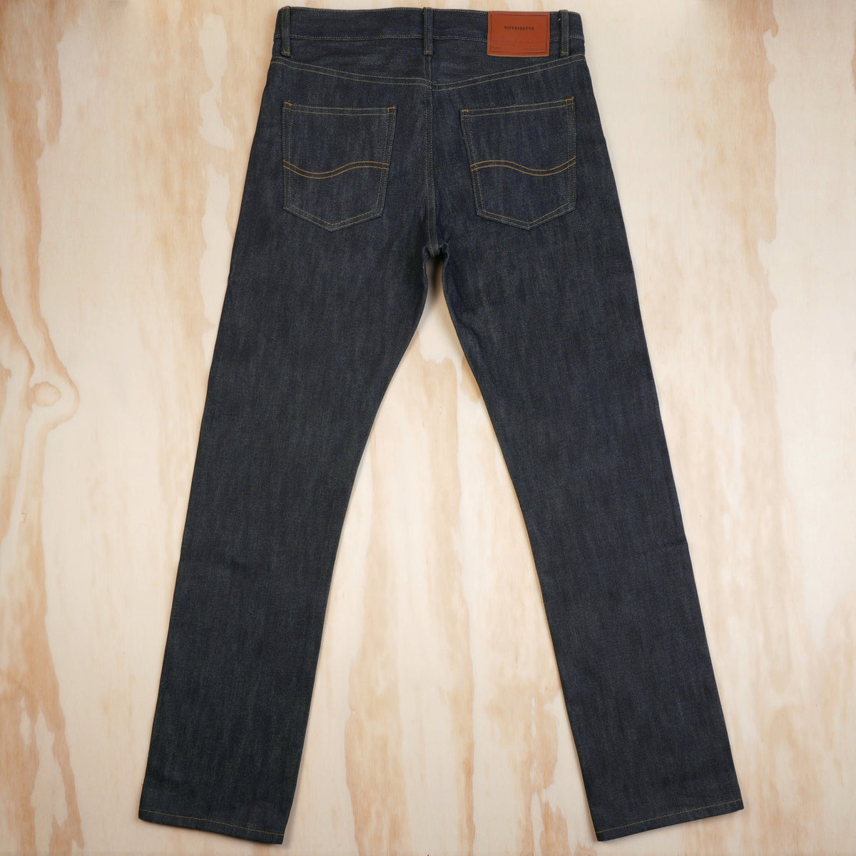 Back view of dark indigo selvedge jeans showing patch pockets and a leather waistband patch.
